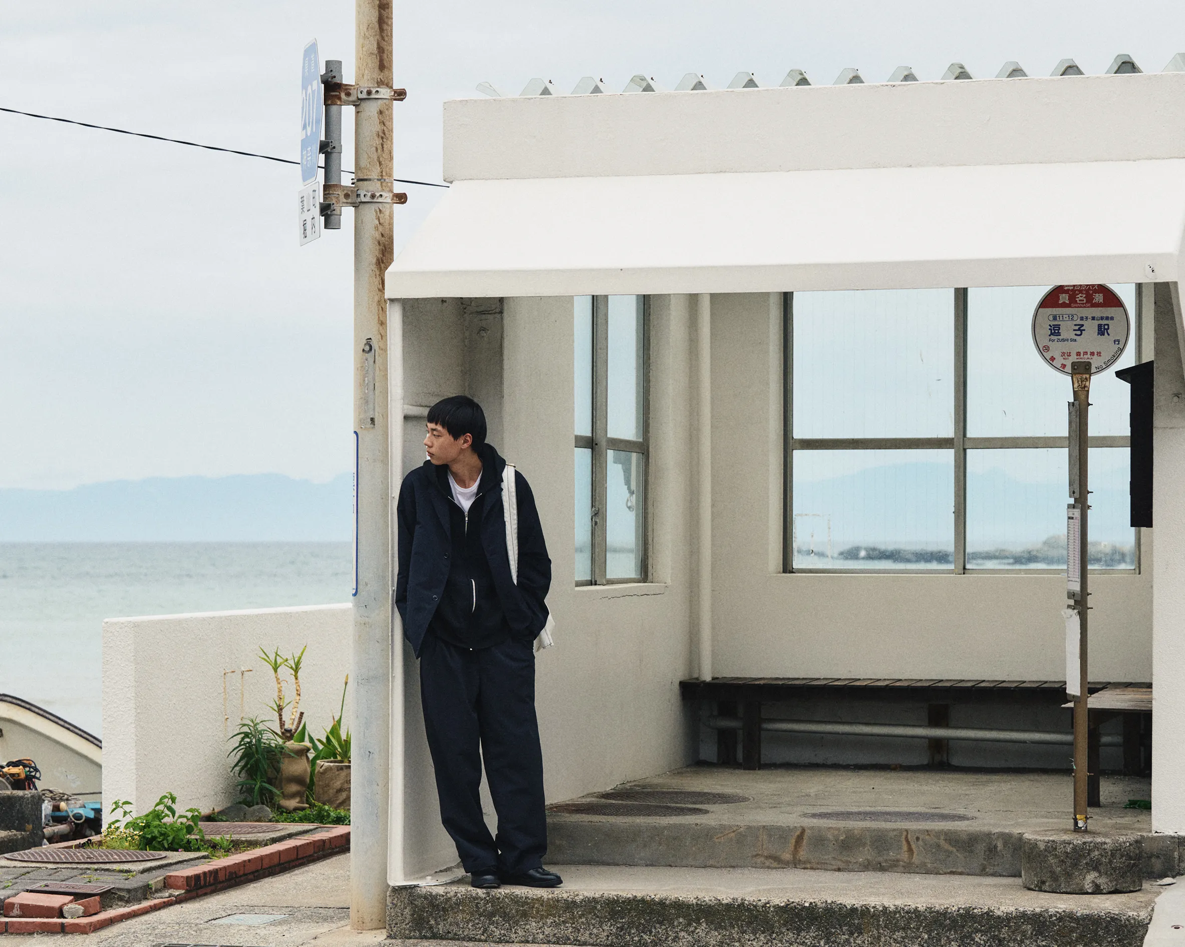 ET058 ORDLY E-BLACK worn with dark tailoring beside a coastal building