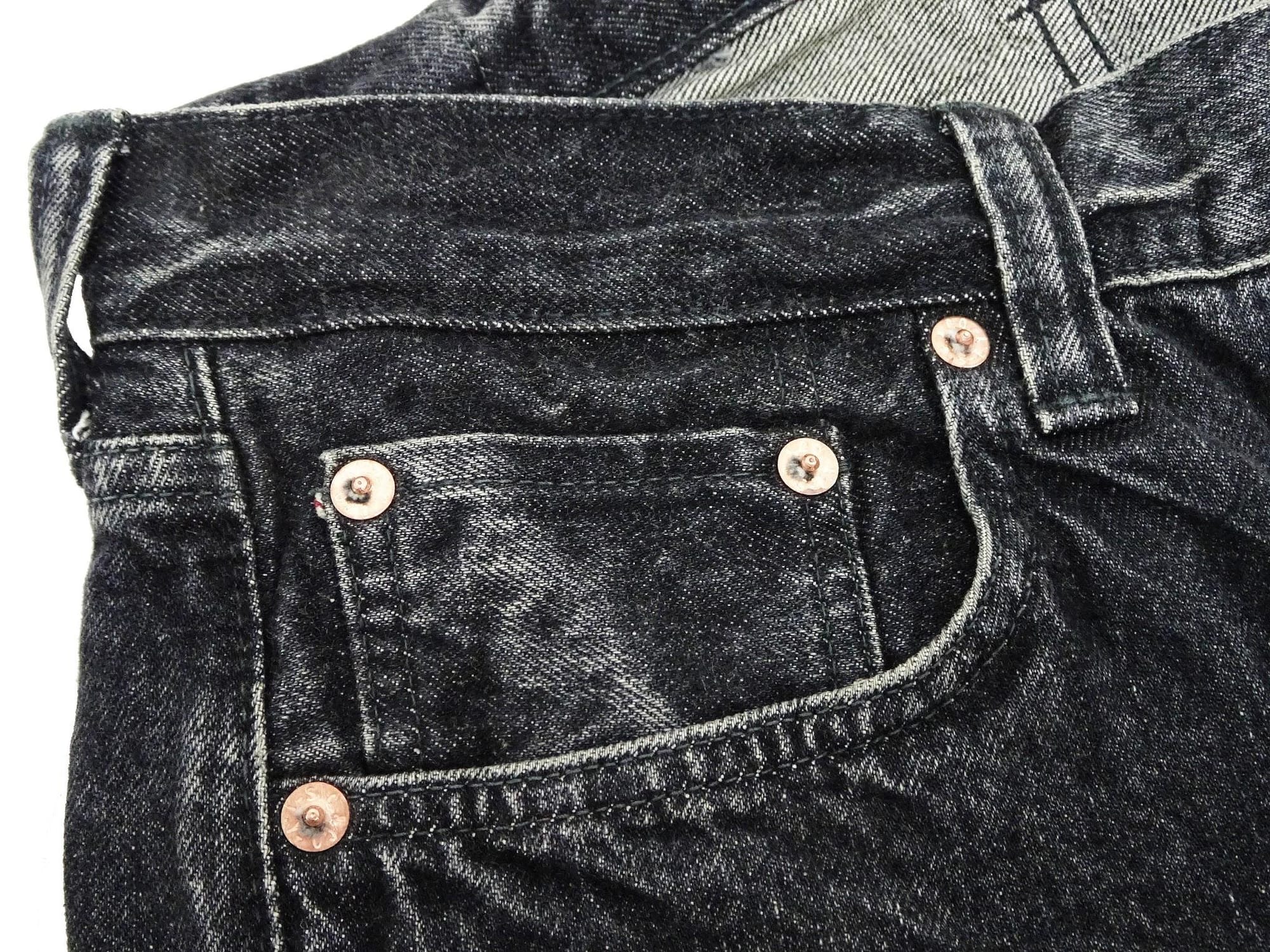 Coin pocket and copper rivets on the worn black jeans.