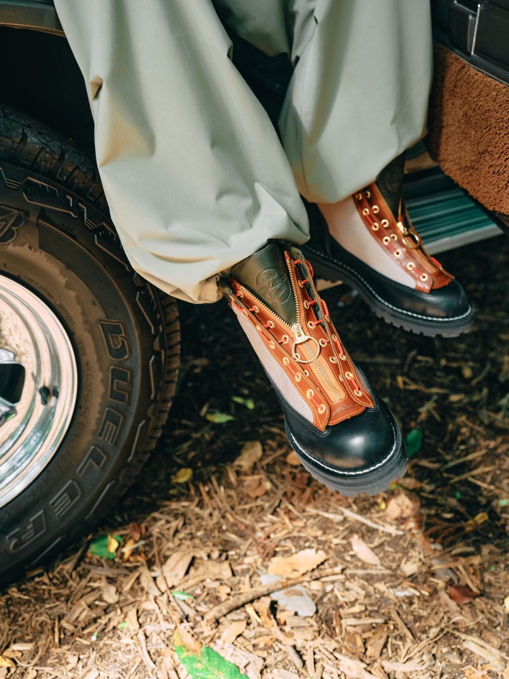 Land Cruiser Field R Overland boots worn beside a vehicle, showing orange zipper units and pale side panels.