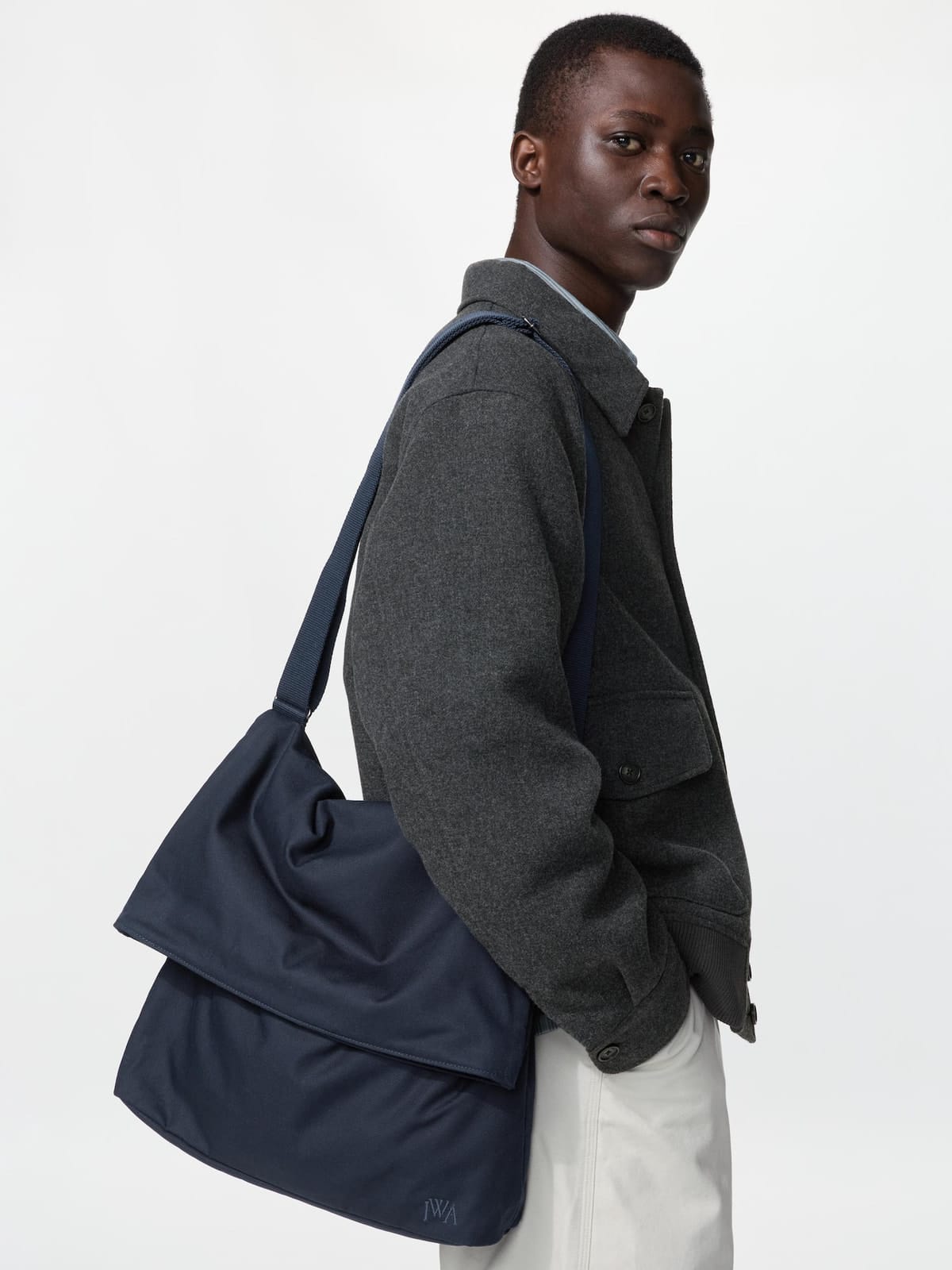 Model carrying the navy JW ANDERSON shoulder bag over a charcoal jacket
