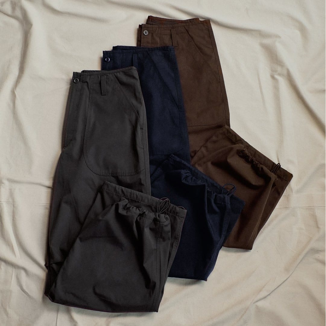 Three colours of GU and Engineered Garments wide utility trousers arranged flat.