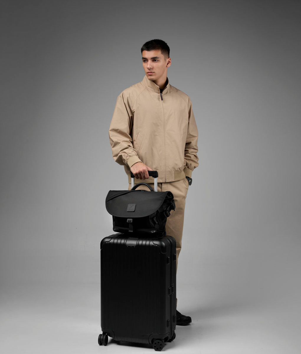 A model holds the 7ven Messenger above a wheeled suitcase.