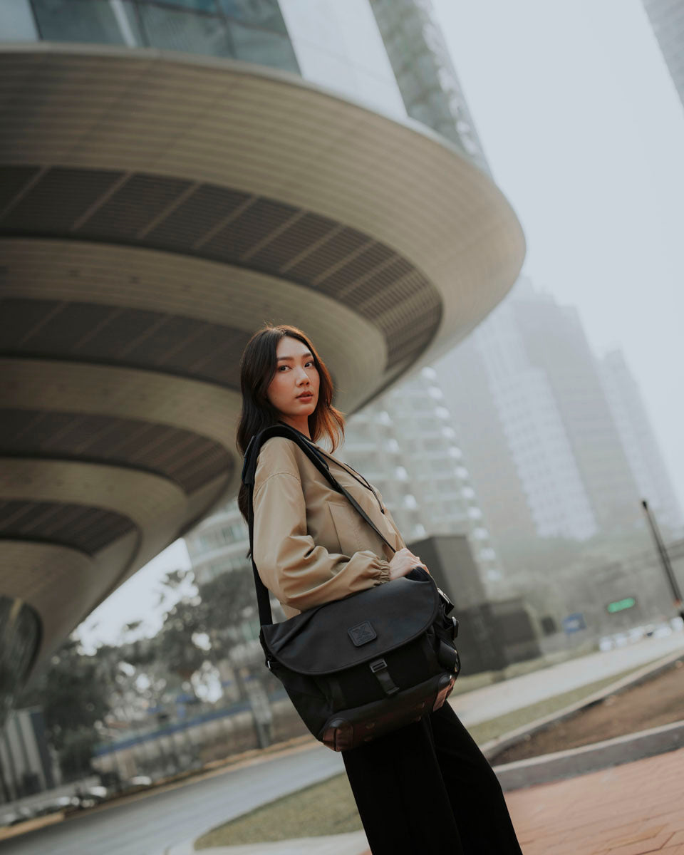 A woman carries the 7ven Messenger beside a concrete building.